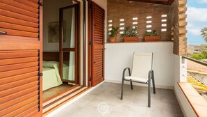 Een balkon met een houten deur, een stoel en bloempotten.