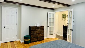 Une chambre à coucher comprenant un lit, une commode, un pouf vert et une porte donnant sur une autre pièce.