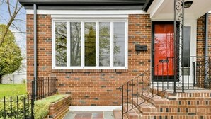 Une maison en briques avec une porte rouge, des fenêtres à cadre blanc et un escalier en métal noir menant à l’entrée.