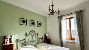 A room with two beds, a chandelier, a window with curtains, and a view of the outdoors. - Il Podere di Casa Rossa Pienza (Pienza)