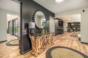A modern living room with a glass-top coffee table, a large mirror, and a wooden accent wall. - Heated Pool. Luxe STR/game room/fire pit/privacy (Mears)