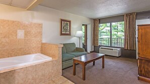 A bathroom with a bathtub, a green patterned sofa, a wooden table, and a window with curtains.