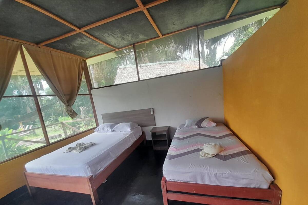 Una habitación con dos camas individuales, una mesita y un ventanal con cortinas.