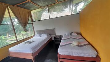 Quarto com duas camas de solteiro, uma mesinha e uma janela com cortinas.
