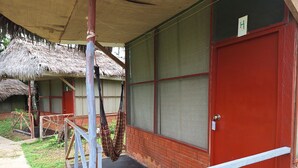 Una construcción con puerta roja, techo de paja y un área cercada con una hamaca.