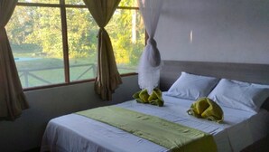 Un dormitorio con cama, ropa de cama blanca, una manta verde y vistas al exterior.
