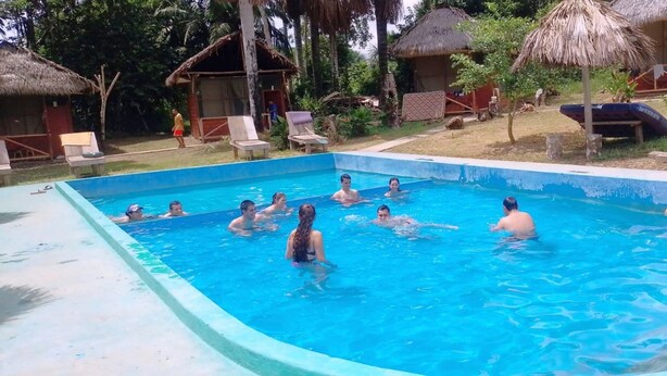 Una piscina rodeada de sillas de descanso y cabañas con techo de paja.