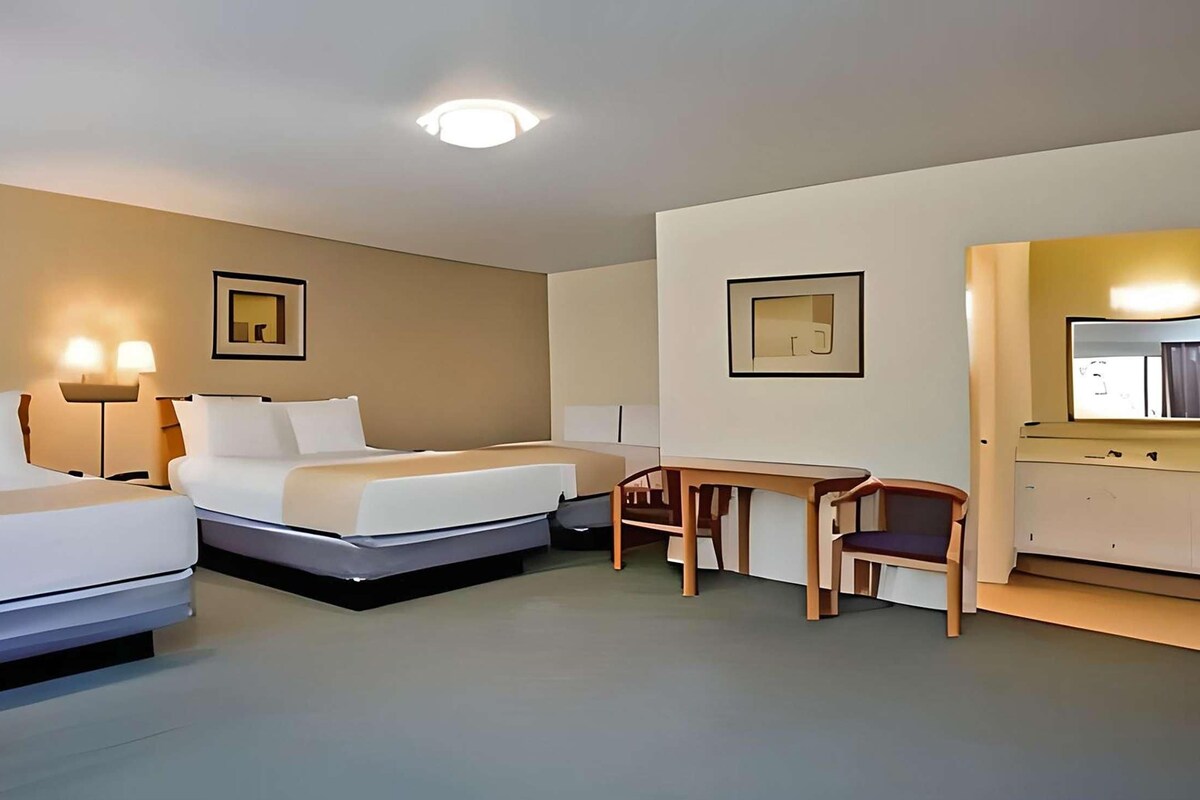 A hotel room with two beds, a desk, a chair, and a mirror.