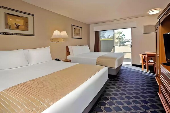 Quarto de hotel com duas camas, uma mesa, uma cadeira e uma televisão.