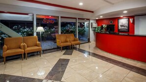 A lobby with a reception desk, two sofas, a lamp, and a staircase. - Travelodge by Wyndham Red Bluff South of Redding (Red Bluff)
