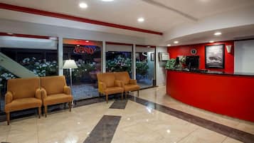 A lobby with a reception desk, two sofas, a lamp, and a staircase.