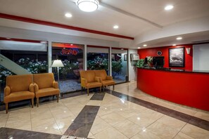 A lobby with a reception desk, two sofas, a lamp, and a staircase. - Travelodge by Wyndham Red Bluff South of Redding (Red Bluff)