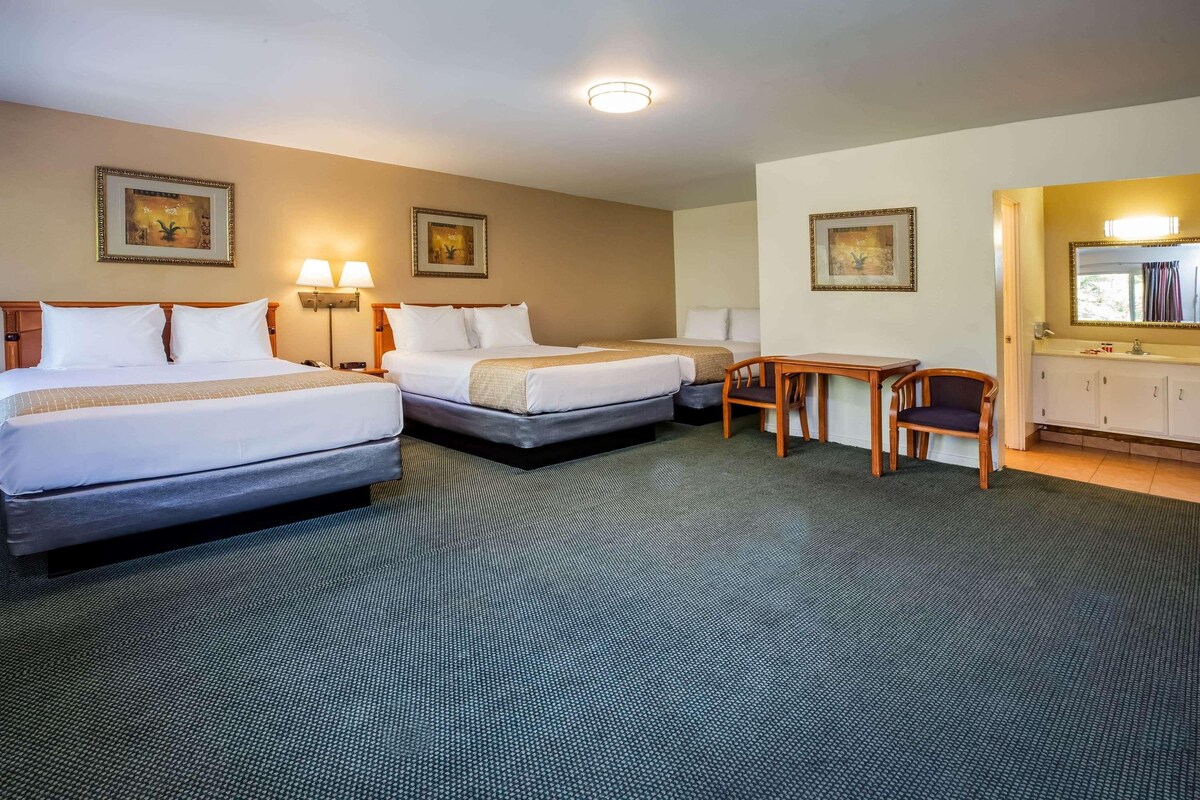 A hotel room with two beds, a desk, a chair, and a bathroom with a mirror and cabinet.