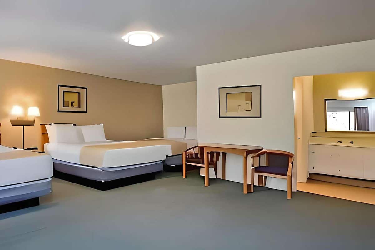 Habitación de hotel con dos camas, un escritorio, una silla y un espejo.