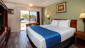 A hotel room with a large bed, a television, a desk, and a view of the outside. - Travelodge by Wyndham Red Bluff South of Redding (Red Bluff)