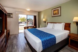 A hotel room with a large bed, a television, a desk, and a view of the outside. - Travelodge by Wyndham Red Bluff South of Redding (Red Bluff)