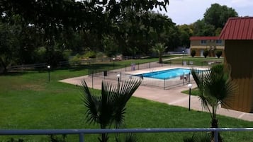 Une piscine entourée d’une zone délimitée par une clôture, avec un bâtiment en arrière-plan.