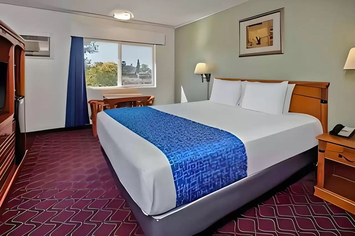 Una habitación de hotel con una cama grande, un escritorio, una silla, una lámpara y una ventana con vistas.