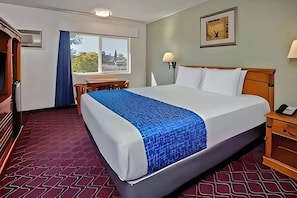A hotel room with a large bed, a desk, a chair, a lamp, and a window with a view. - Travelodge by Wyndham Red Bluff South of Redding (Red Bluff)