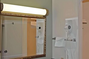 A bathroom with a large mirror, a hairdryer, and a towel rack. - Travelodge by Wyndham Red Bluff South of Redding (Red Bluff)