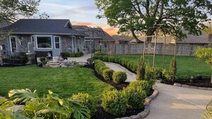 A residential backyard with a stone pathway, manicured lawn, and a wooden fence. - The Cunningham Cottage | King Bed & Garden (Springfield)