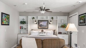 A bedroom with a bed, a ceiling fan, a bedside table, a lamp, and a chair. - The Cunningham Cottage | King Bed & Garden (Springfield)