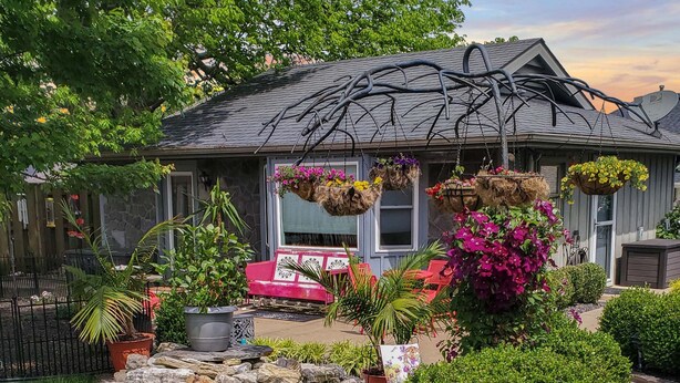 A house with a stone patio, a red bench, hanging flower baskets, and a garden with various plants. - The Cunningham Cottage | King Bed & Garden (Springfield)