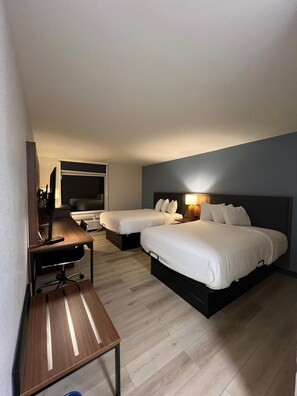Ein Hotelzimmer mit zwei Betten, einem Schreibtisch, einem Stuhl, einem Fernseher und einer Lampe.