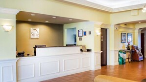 Ein Hotel-Empfangsbereich mit einer Rezeption, einem Schild mit der Aufschrift 'Sleep Inn Suites' und einer kleinen Sitzecke mit einer Couch.