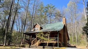 A log cabin with a porch, surrounded by tall trees.
