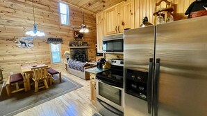 A wooden cabin interior with a dining area, kitchen, and a fireplace.