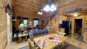 A cabin interior with a wooden dining table, a sofa, a staircase, and a kitchen area.