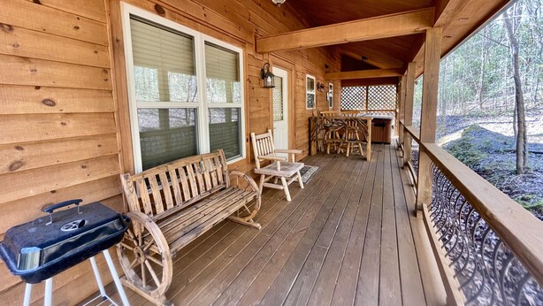 A wooden porch with a bench, chairs, and a grill.