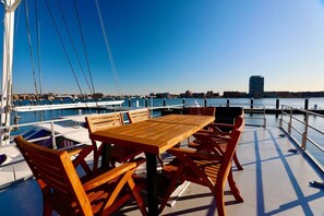 A wooden table and chairs on a boat deck with a view of a marina and buildings in the background.
