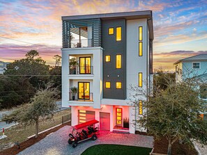 A modern two-story building with multiple balconies, a red carport, and a well-maintained lawn. - 30A Luxury New Build| Private Htd Pool | Views | Steps to Beach|Golf Cart |Bikes (Santa Rosa Beach)
