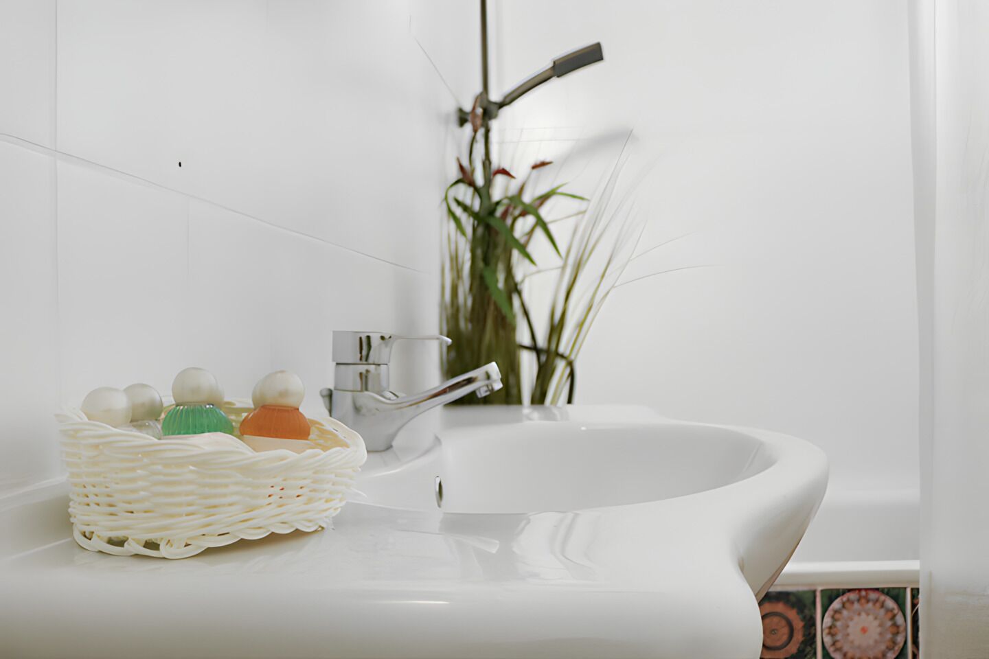 Un baño con un lavamanos blanco, un grifo plateado y una bañera blanca. Hay una cesta de mimbre con artículos de aseo en el lavamanos.