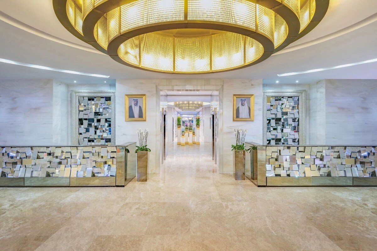 A hotel lobby with a central walkway, reception desks, and framed portraits on the walls.