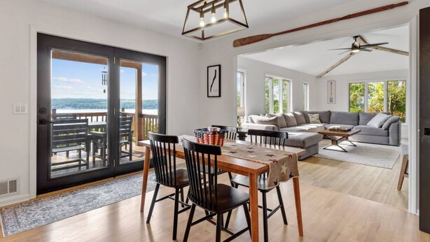 A spacious living area with a dining table, chairs, and a sofa. There is a large window providing a view of the outdoors.