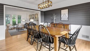 A dining area with a wooden table and chairs, a chandelier, and a view of a living room with a sofa and a lamp.