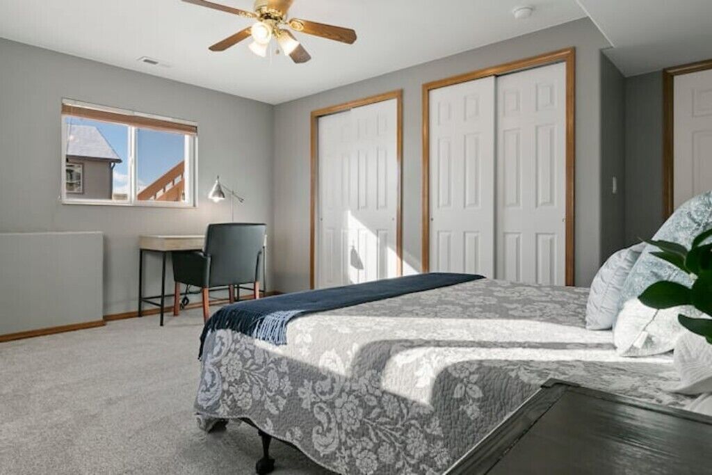 Une chambre à coucher avec un lit, un bureau et une chaise. Il y a deux portes et une fenêtre.