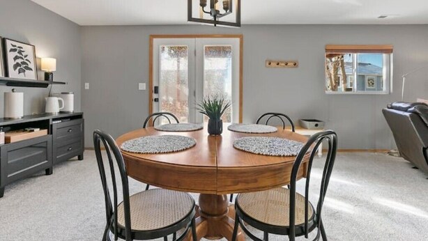 Un comedor con una mesa de madera, cuatro sillas, una araña y vistas al exterior a través de una puerta.