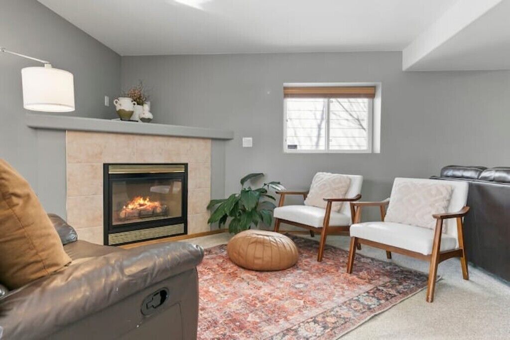 A living room with a fireplace, two white armchairs, a leather sofa, a patterned rug, and a large plant.