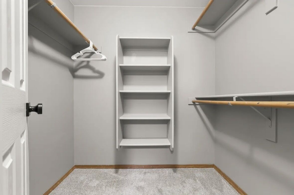 Un couloir étroit avec une porte blanche, un cadre de porte en bois et une étagère blanche à trois niveaux.