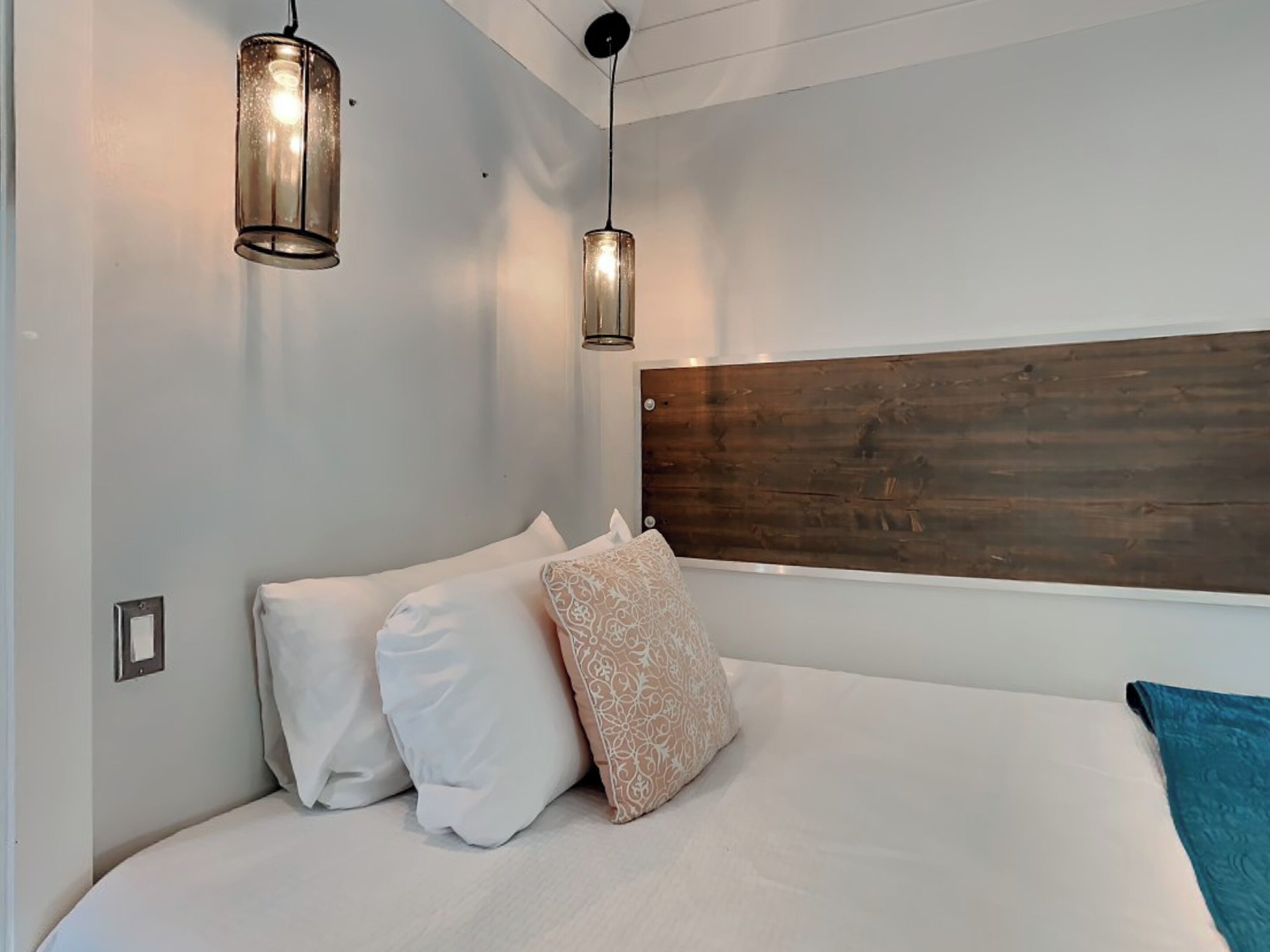 Quarto com uma cama grande, duas luzes fixadas na parede e cabeceira de madeira.