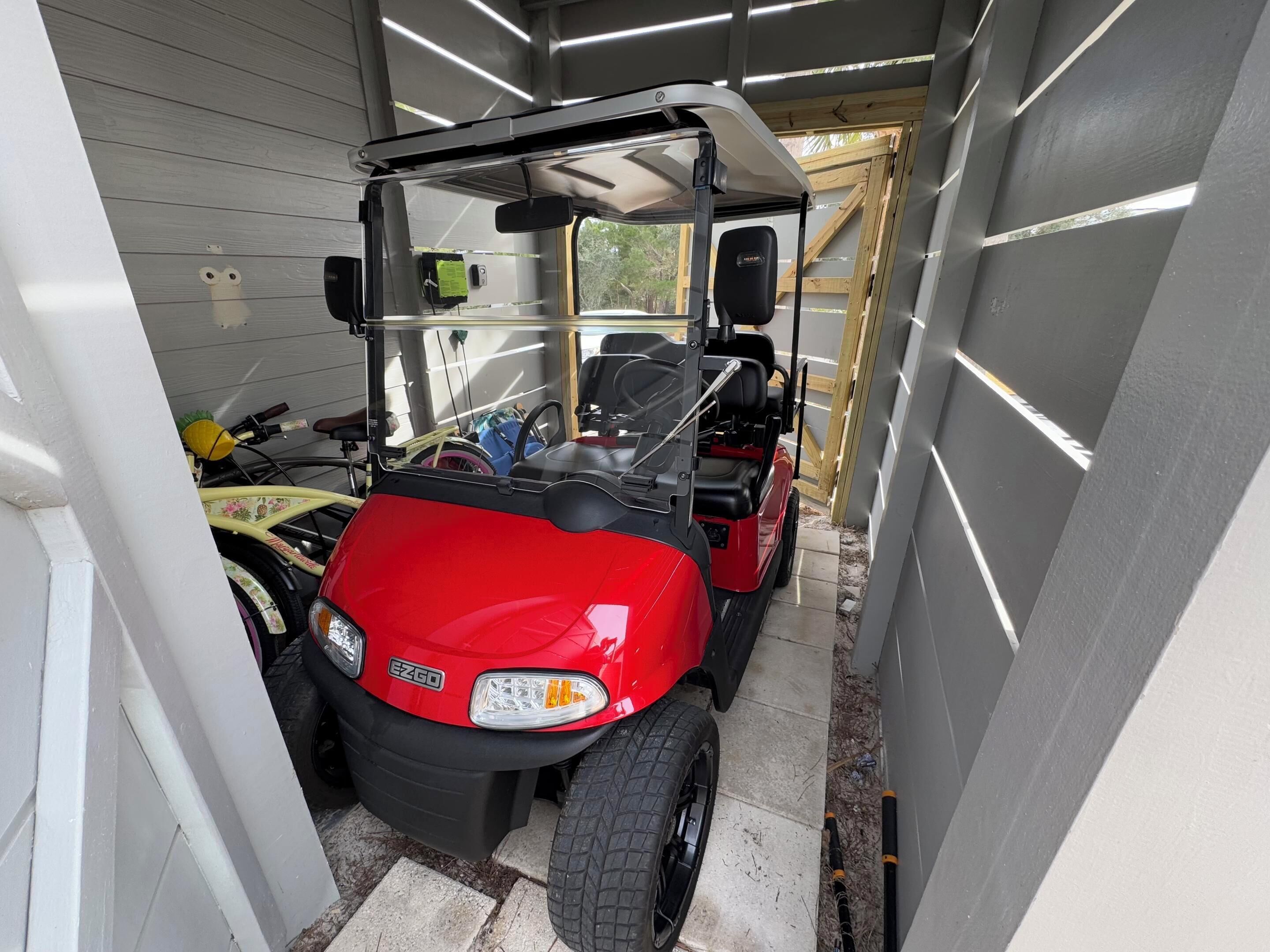 Un carrito de golf rojo estacionado dentro de un garaje estrecho con piso de madera y paredes de metal.