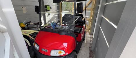 Un carrito de golf rojo estacionado dentro de un garaje estrecho con piso de madera y paredes de metal.