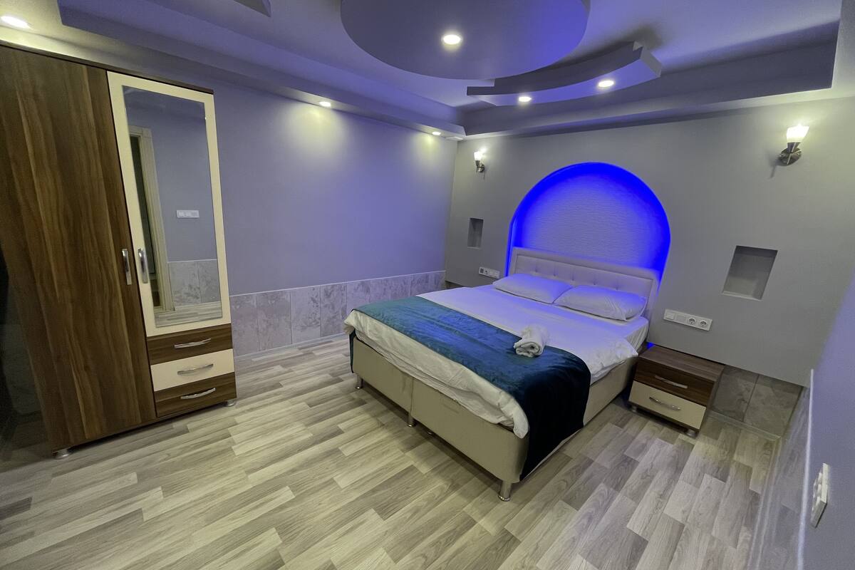 Ein modernes Schlafzimmer mit Bett, Nachttischen, einem Kleiderschrank und einer markanten, blau beleuchteten Wandnische.