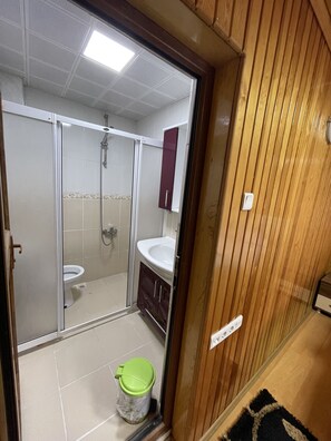 Ein Badezimmer mit Duschkabine aus Glas, einem weißen Waschbecken und einer Holzeinrichtung.