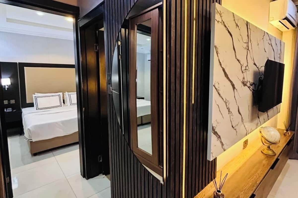 Une chambre d’hôtel moderne équipée d’un lit, d’une télévision, d’une console en bois et d’un mur en marbre.