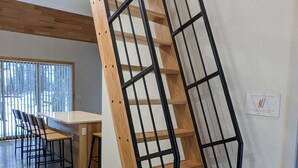 A modern staircase with wooden steps and black metal railings, leading to a dining area with a large table and chairs. - Fox Cabin @ Orange Tractor Retreat: 3BR ADA accessible cabin on 40 wooded acres (Wisconsin Dells)